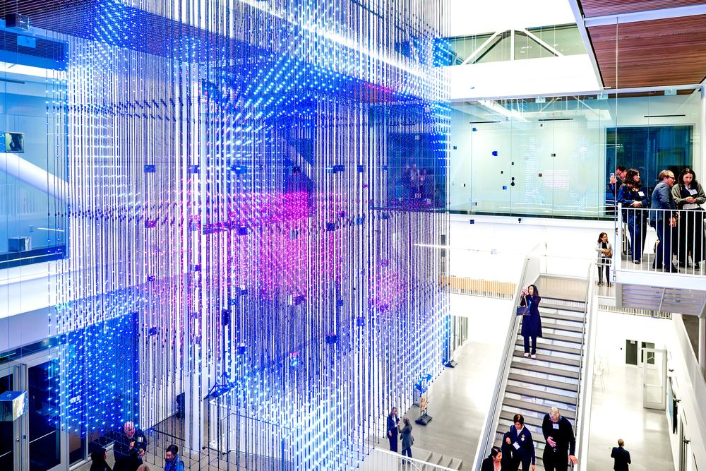 The Strauch Hypercube lit blue and violet above visitors on the atrium stairs