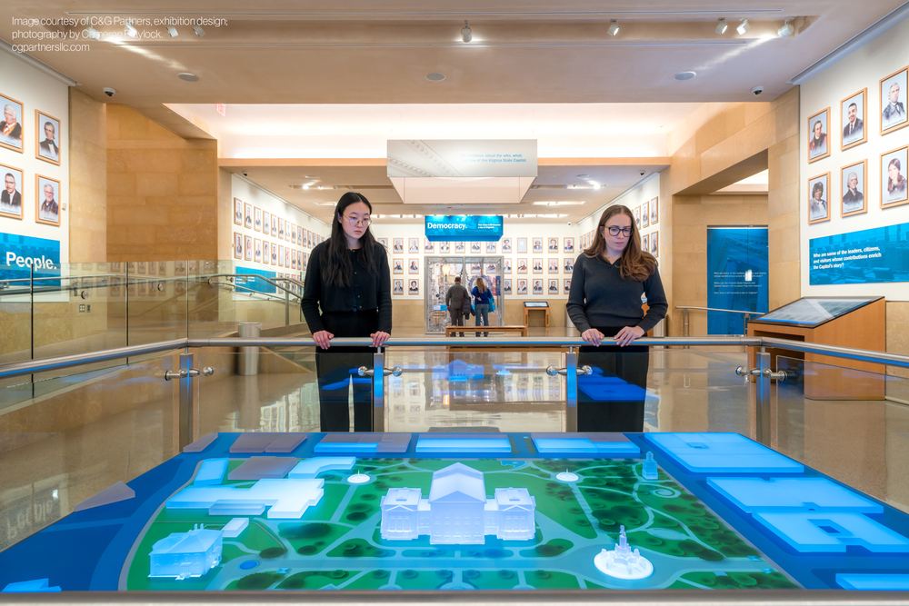 Two visitors at the Virginia Capitol LED table showing the illuminated grounds model