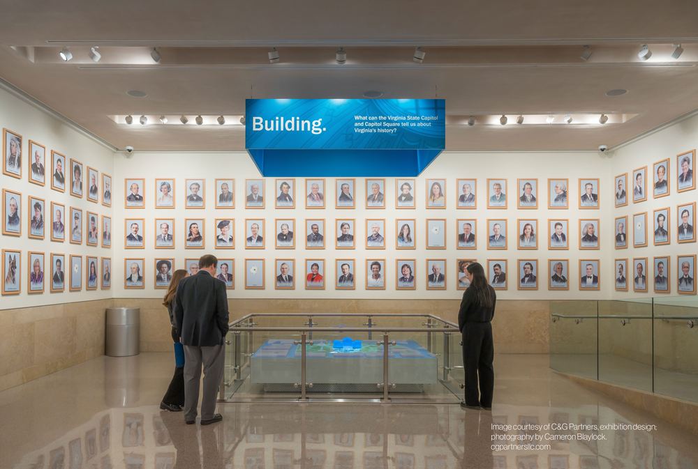 The Virginia Capitol exhibit room, portrait wall framing visitors at the interactive table