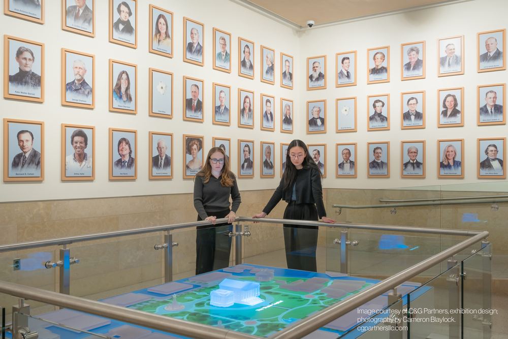 Two visitors at the Virginia Capitol interactive table beneath the wall of portraits