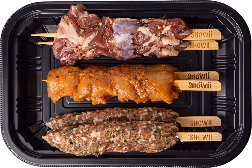 Three wooden skewers with different marinated meats in a black plastic tray, labeled Showii.