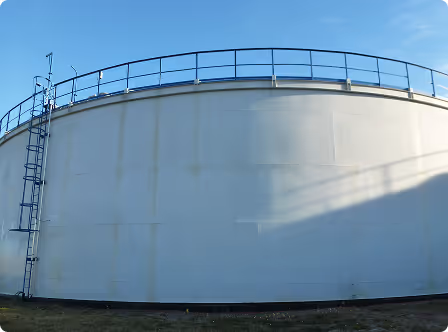 Großer weißer Lagertank mit Metallleiter und Geländer unter blauem Himmel.
