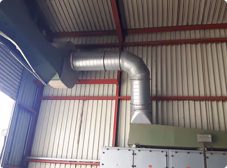 Industrielle Metallbelüftung mit gebogenem Rohr in einer Halle mit rotem Stahlträgerrahmen.