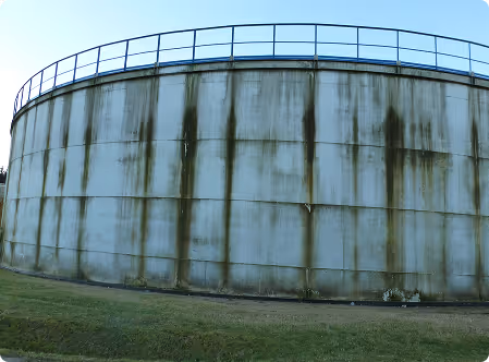 Großer zylindrischer, mit grünem Bewuchs und Flecken bedeckter Wassertank aus Beton mit einem Geländer oben.