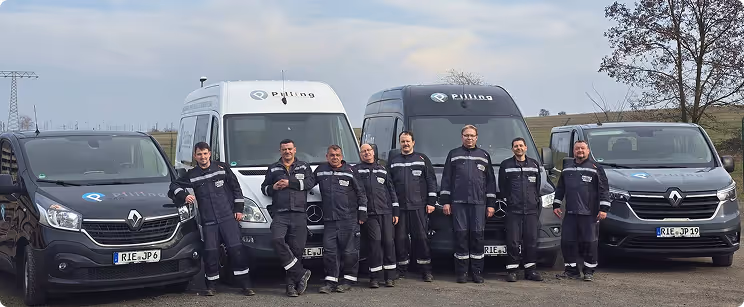 Acht Handwerker in blauen Arbeitsanzügen stehen vor vier Firmenfahrzeugen mit dem Logo 'Pullino' auf einer offenen Fläche bei bewölktem Himmel.