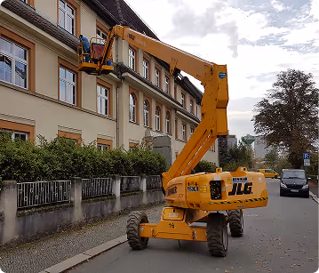 Gelbe Teleskoparbeitsbühne vor einem Wohnhaus an einer Straße mit Bäumen und parkenden Autos.