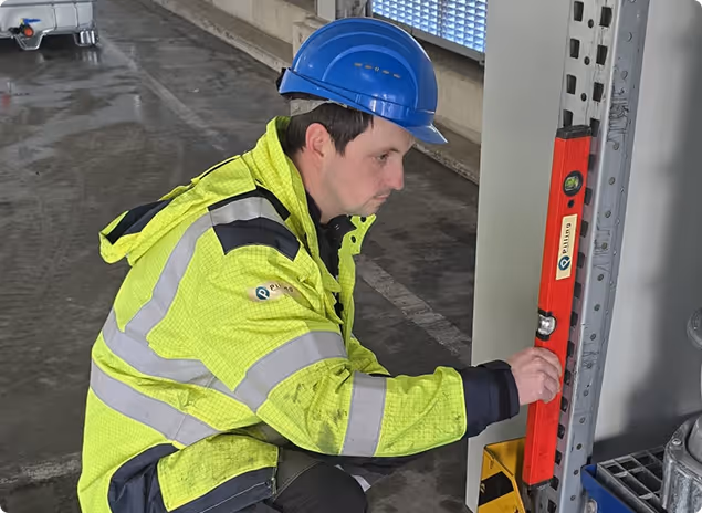 Bauarbeiter mit blauem Helm und gelber Warnjacke nutzt eine Wasserwaage an einem Metallregal in einer Garage.