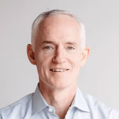 Portrait of a smiling middle-aged man with short gray hair wearing a light blue shirt.