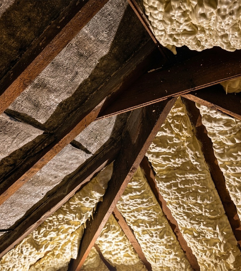 Close-up of attic roof insulation with foam filling spaces between wooden beams.