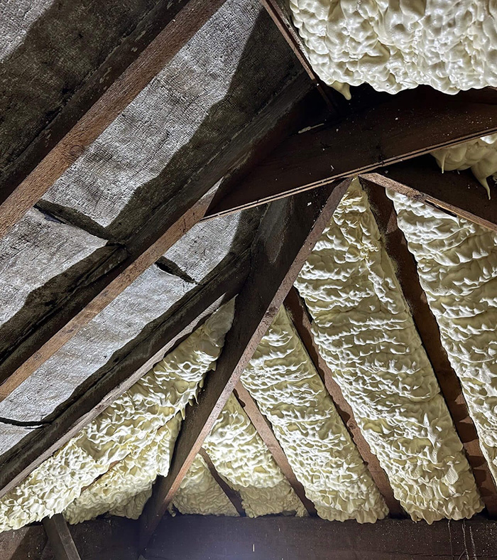 Attic roof with wooden beams partially insulated with white spray foam insulation.