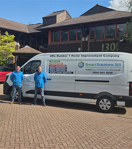 Two men in blue jackets stand beside a white Smart Solutions 365 home improvement van outside a building.