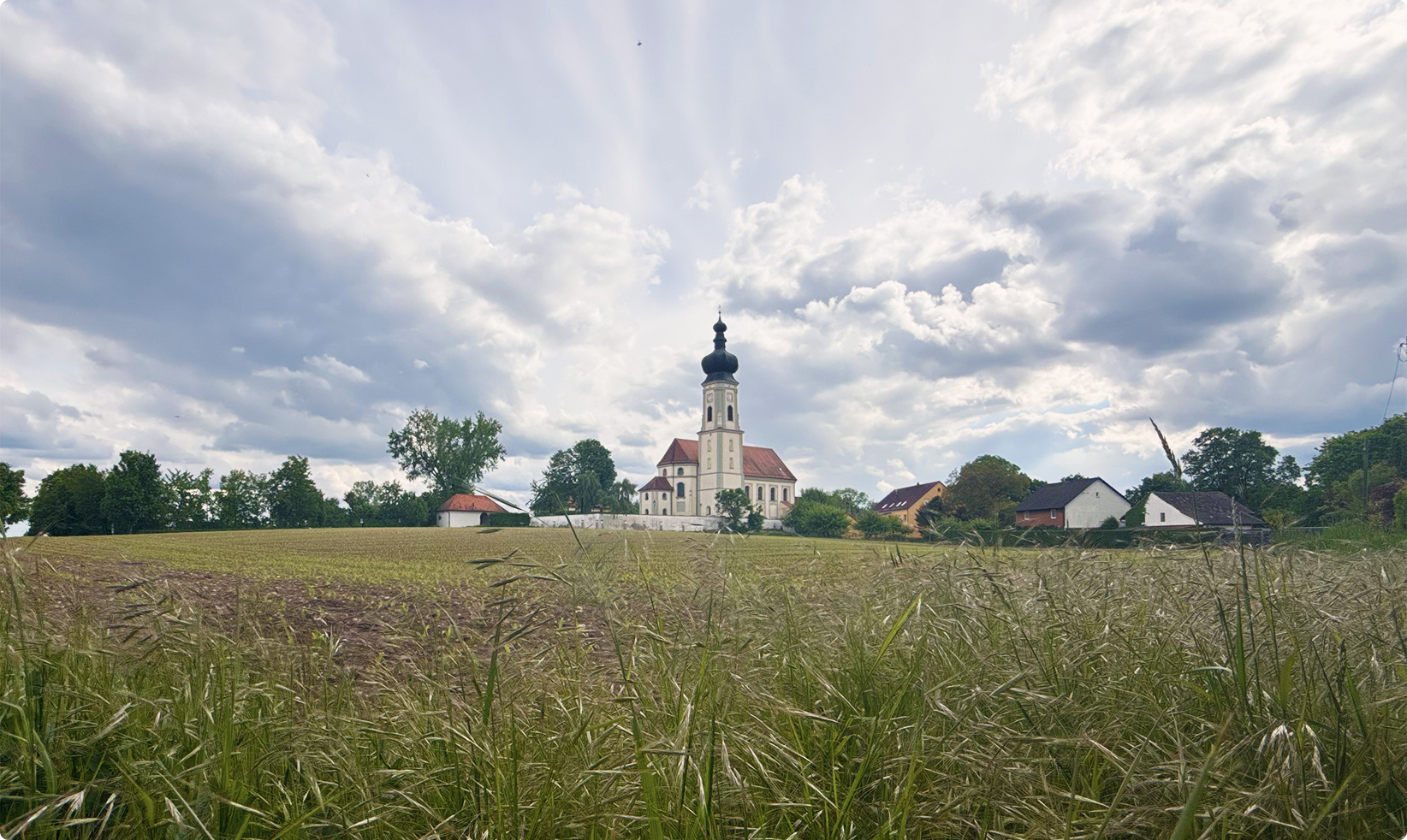 Kirche mit Zwiebelturm in einer ländlichen Umgebung unter bewölktem Himmel.
