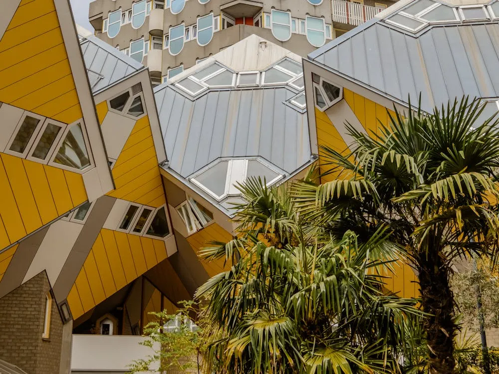 Angular yellow and gray modern cube houses with distinctive tilted windows and palm trees in the foreground.