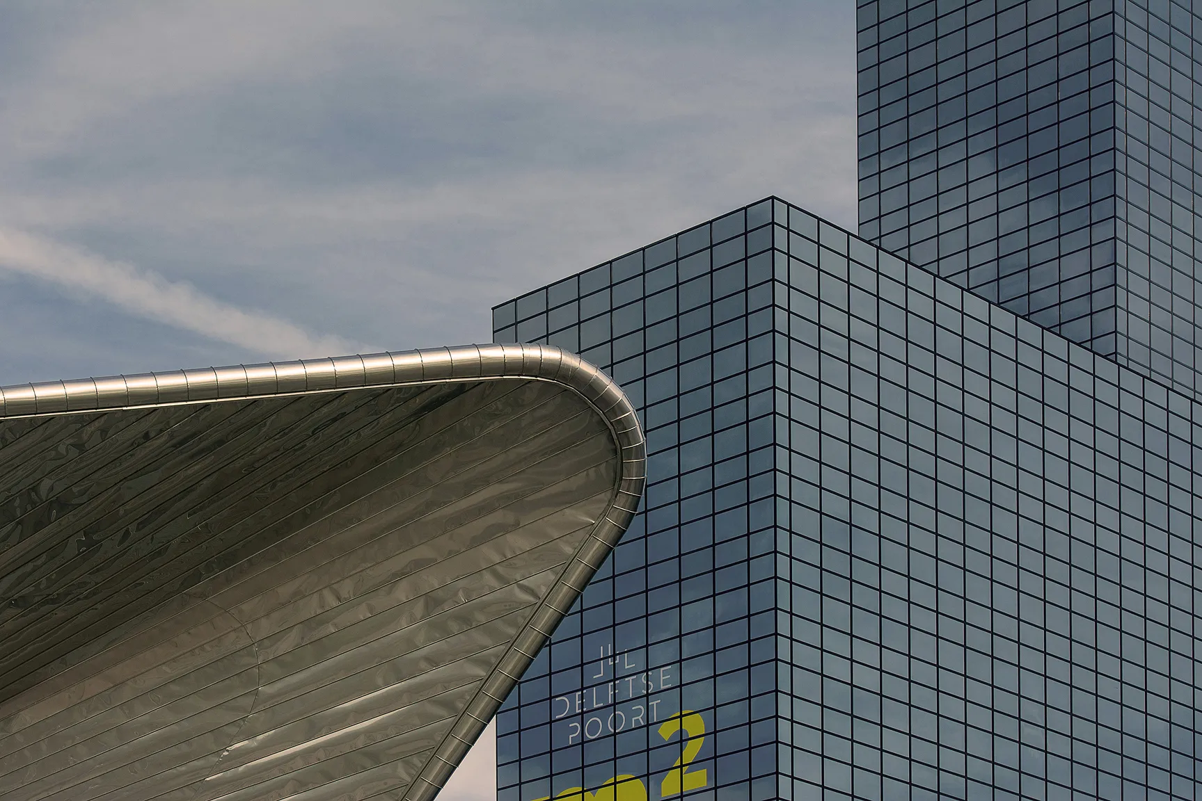 Modern glass skyscraper with the text 'JIL DELFTSE POORT' partially visible, beside a curved metallic architectural structure.