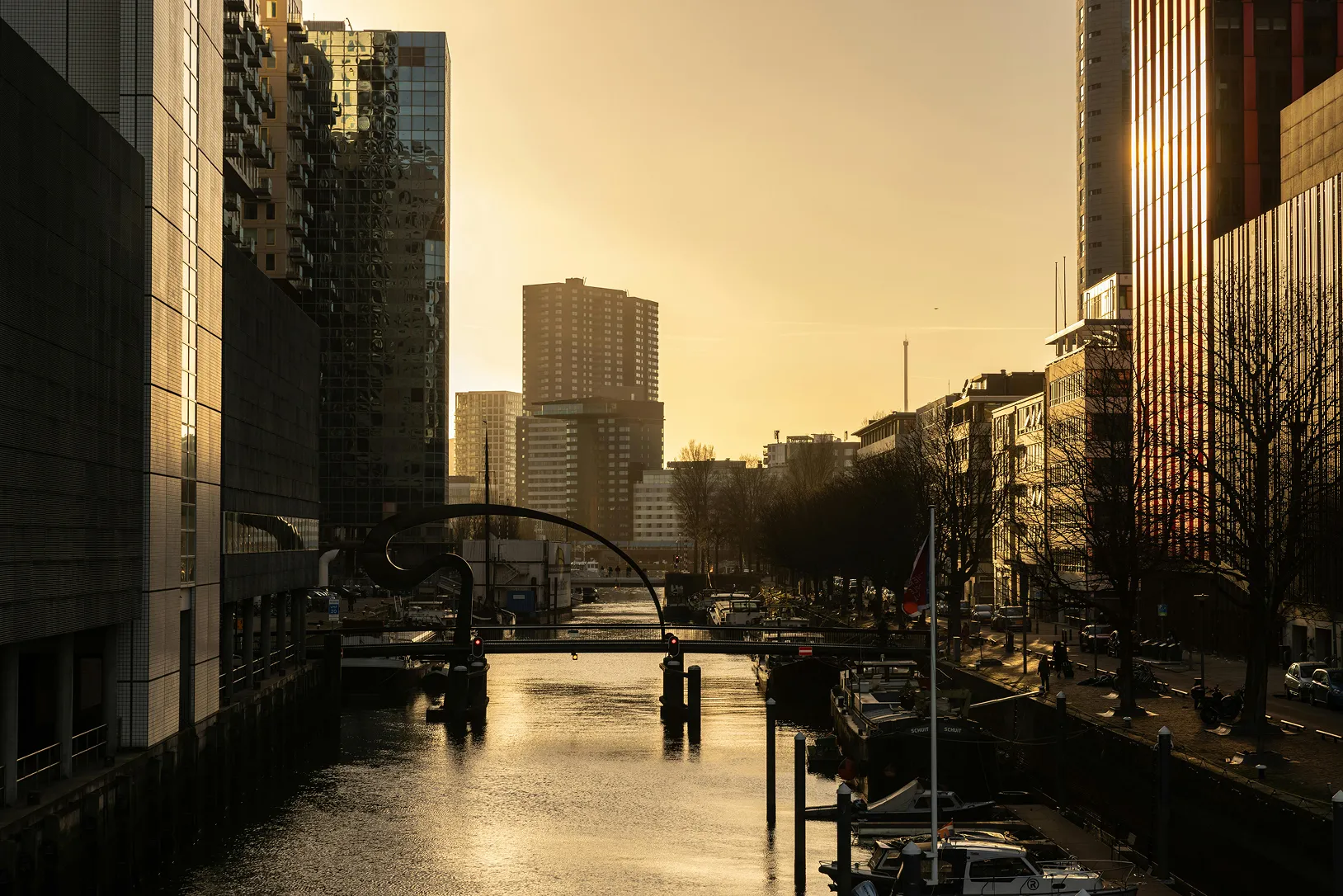 Sunset over a canal lined with modern buildings and boats docked along the sides.