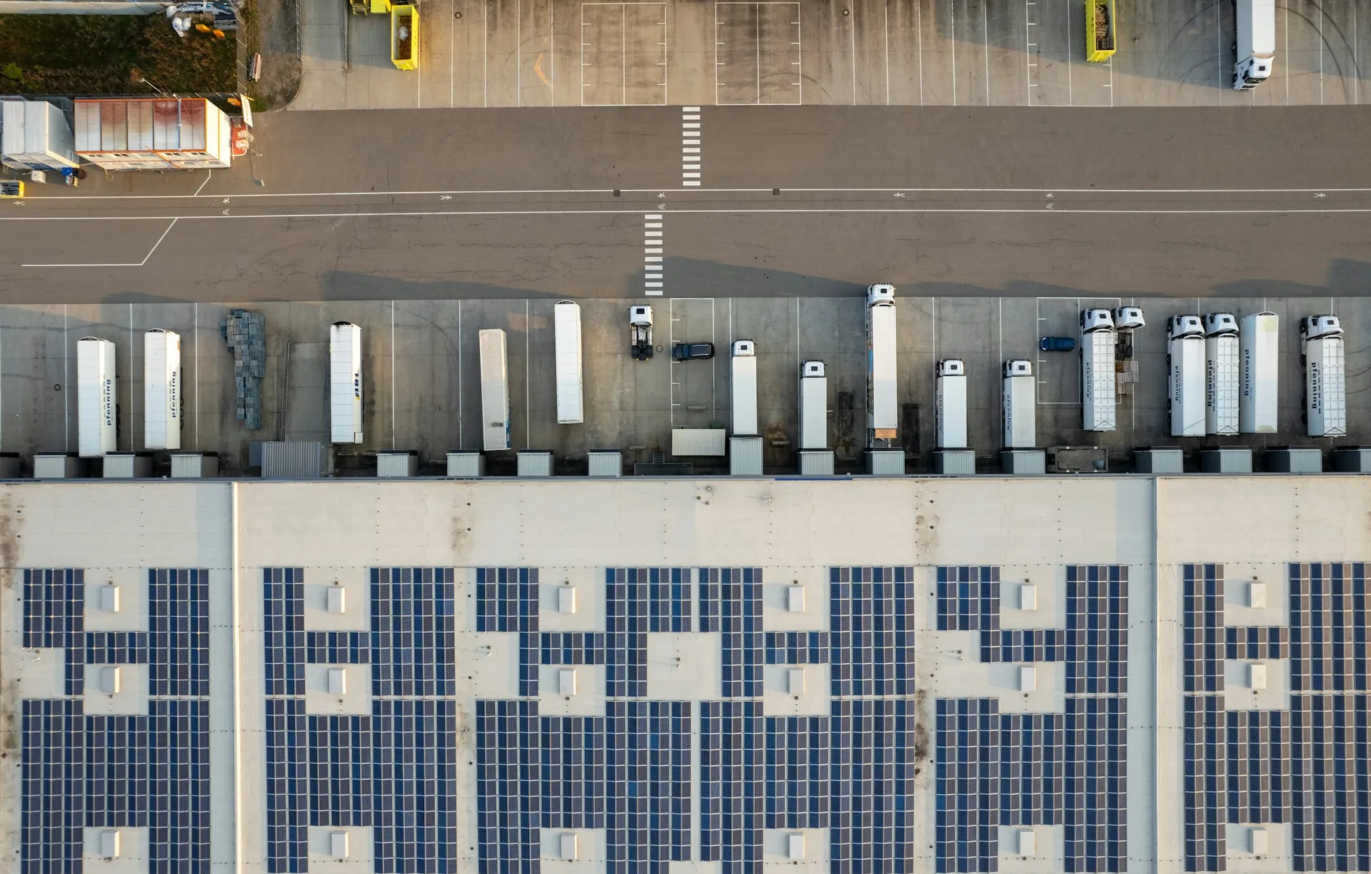 Aerial view of a warehouse rooftop covered with solar panels, with trucks parked at loading docks.