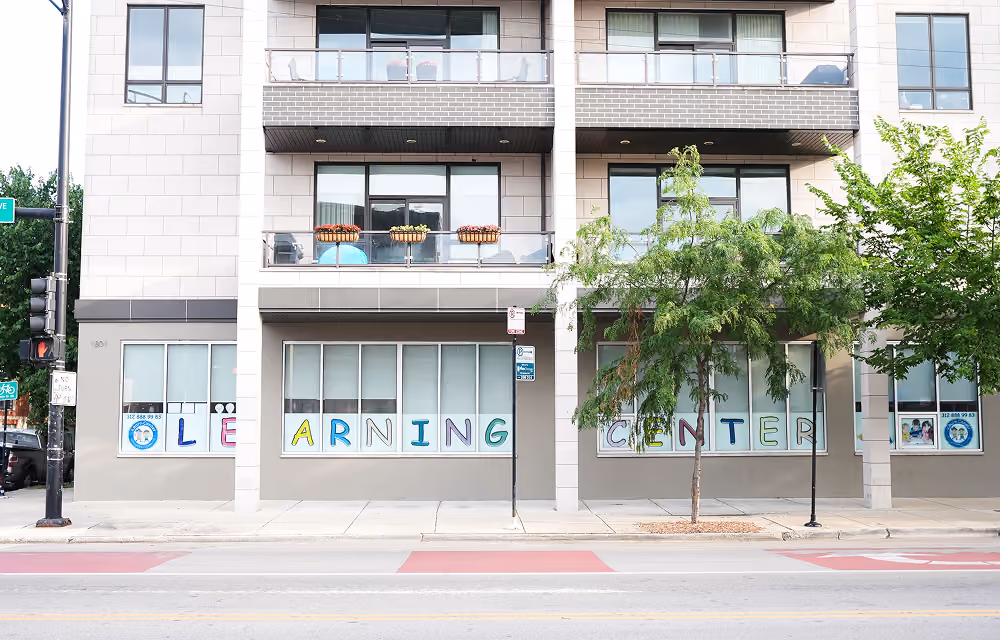Front view of a modern building with large windows displaying colorful letters spelling 'LEARNING CENTER'.
