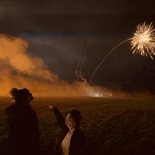A beaver drinking water from a pond in a forest with a woman crouching nearby and a metal animal trap cage beside her.