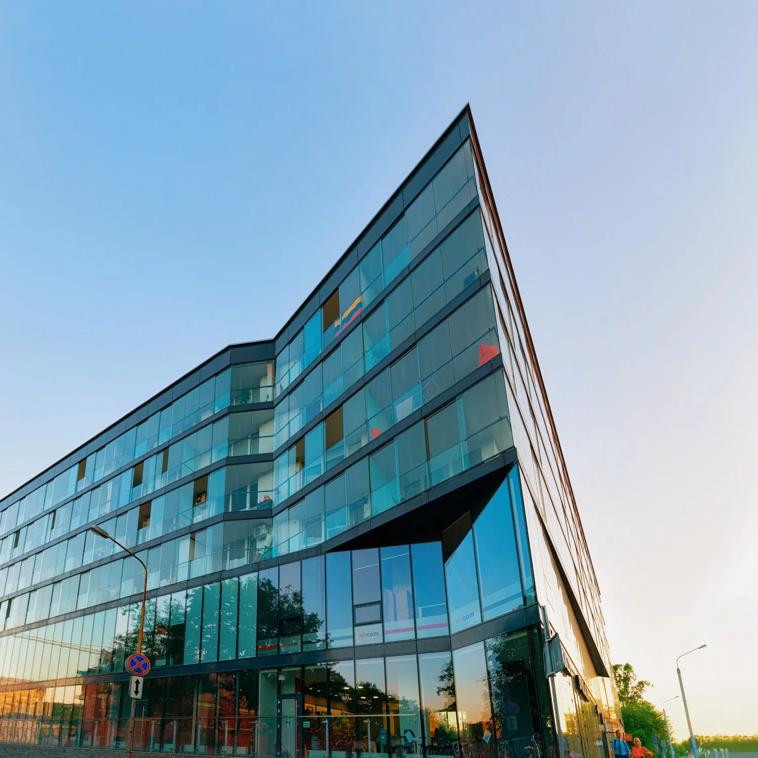 Modern glass office building with reflective blue-tinted windows under a clear sky at sunset.