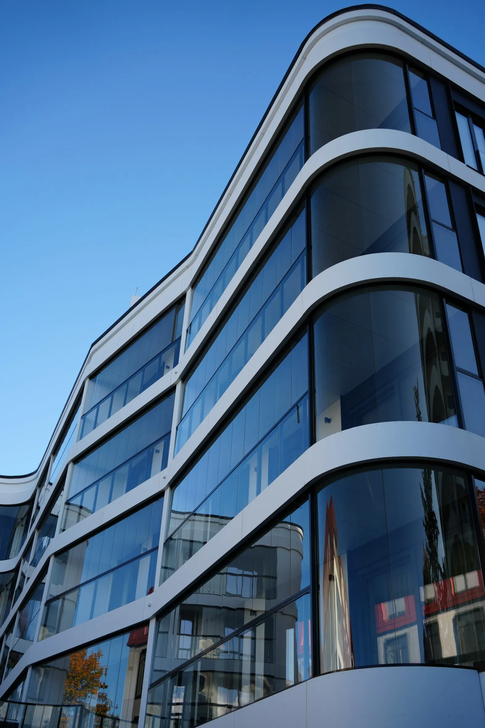 Modern building with curved white horizontal bands and large reflective glass windows under clear blue sky.