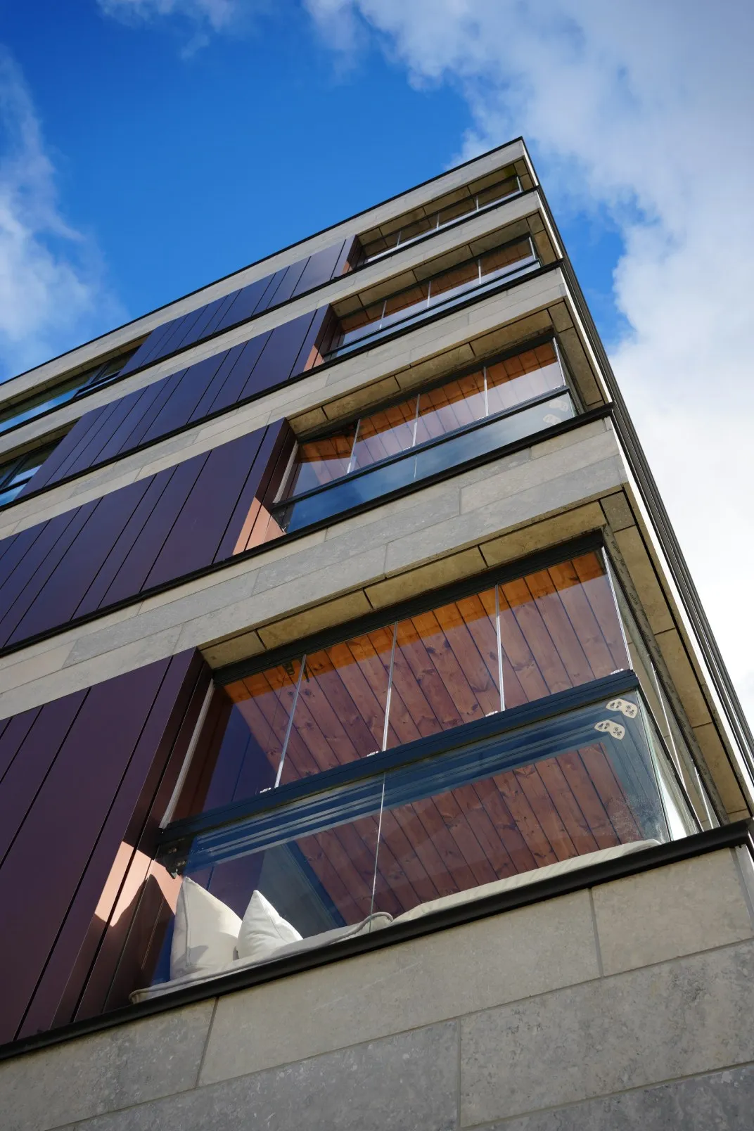 Low-angle view of a modern building corner with glass balconies and a blue sky background.
