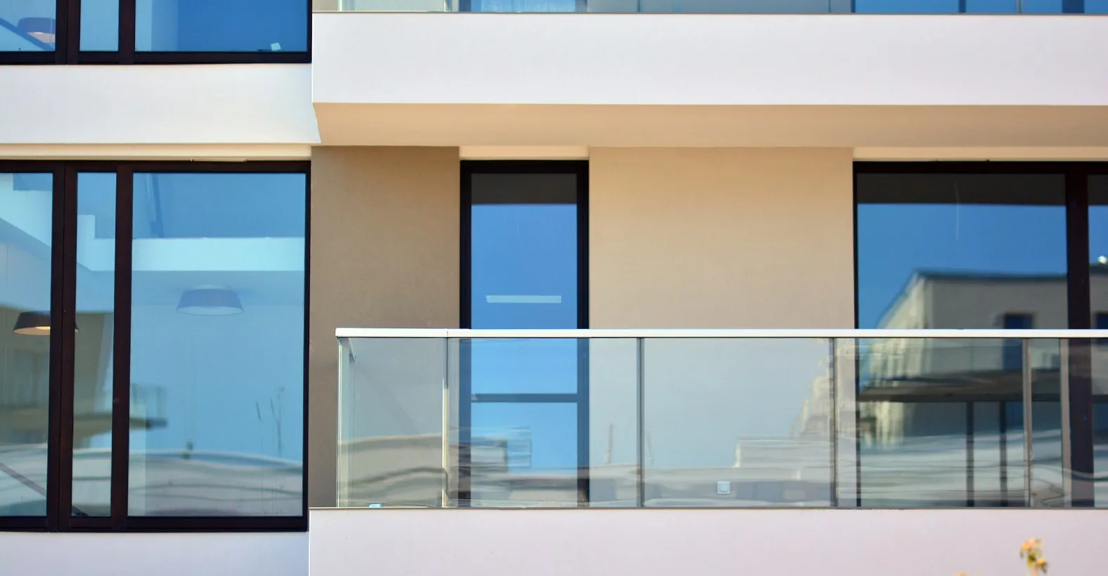 Modern building facade with large windows and a glass balcony railing reflecting the sky.