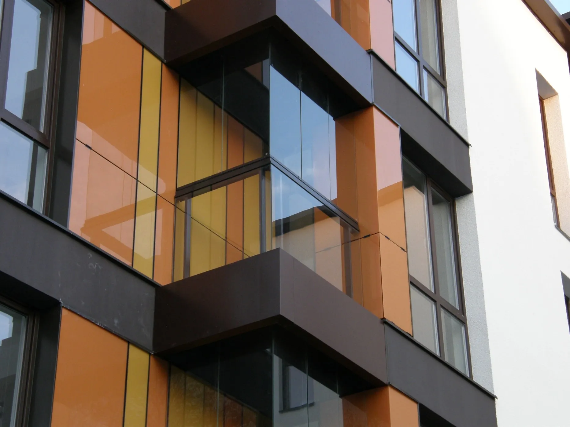 Modern building facade with glass balcony and vertical panels in orange and yellow tones.