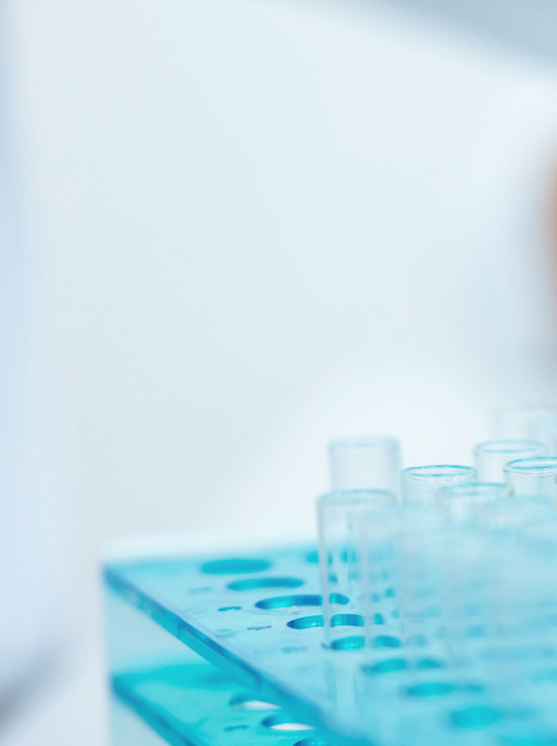 Empty glass test tubes resting in a turquoise plastic rack against a soft white laboratory background