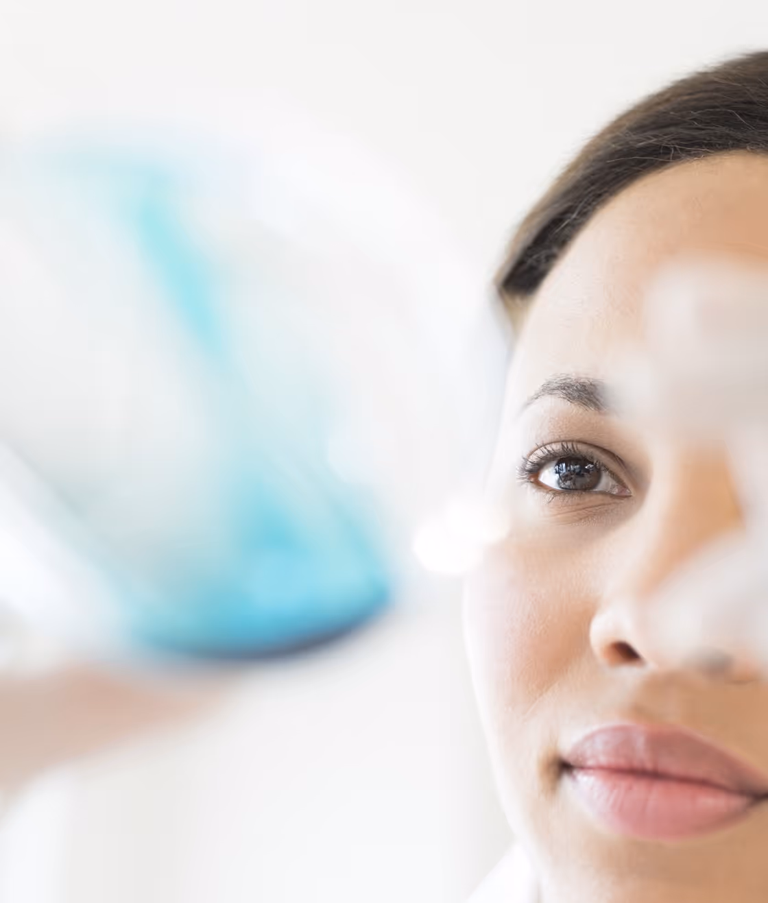 Close-up of a researcher inspecting a blurred laboratory glassware sample held in front of her face