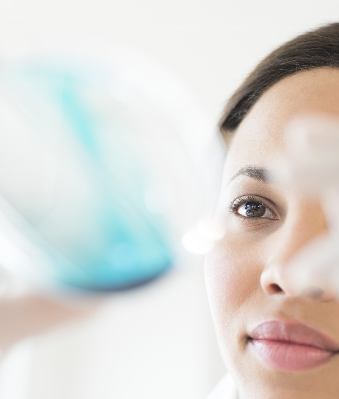 Close-up of a researcher inspecting a blurred laboratory glassware sample held in front of her face
