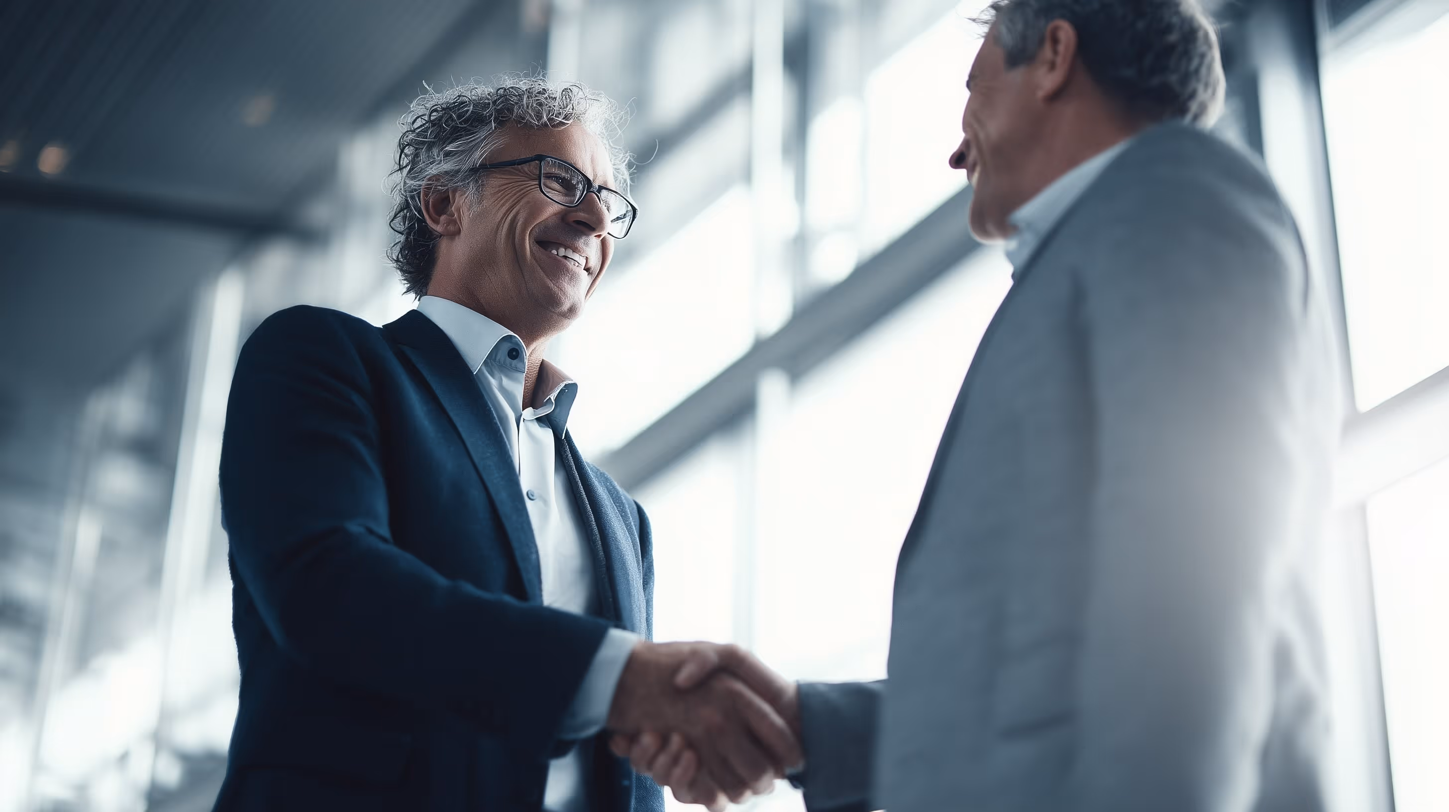 Two male engineers wearing hard hats and work jackets reviewing a tablet outdoors with wind turbines in the background.