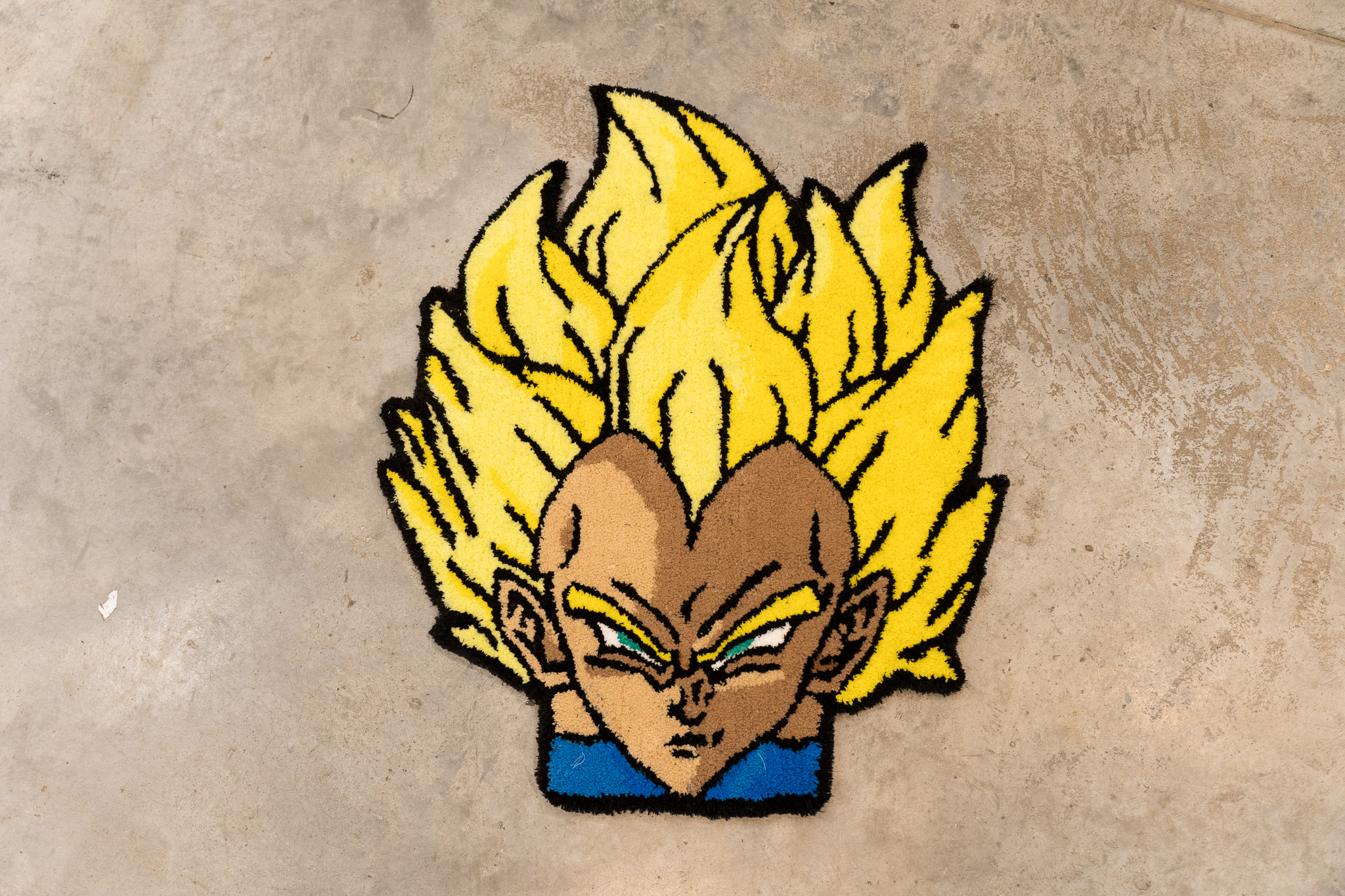 Rug depicting an animated character with large yellow hair and an intense expression on a concrete floor.