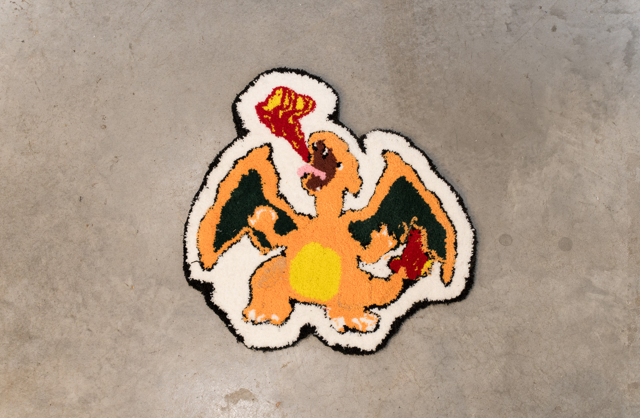 A colorful rug featuring a cartoon orange dragon breathing fire on a gray floor.