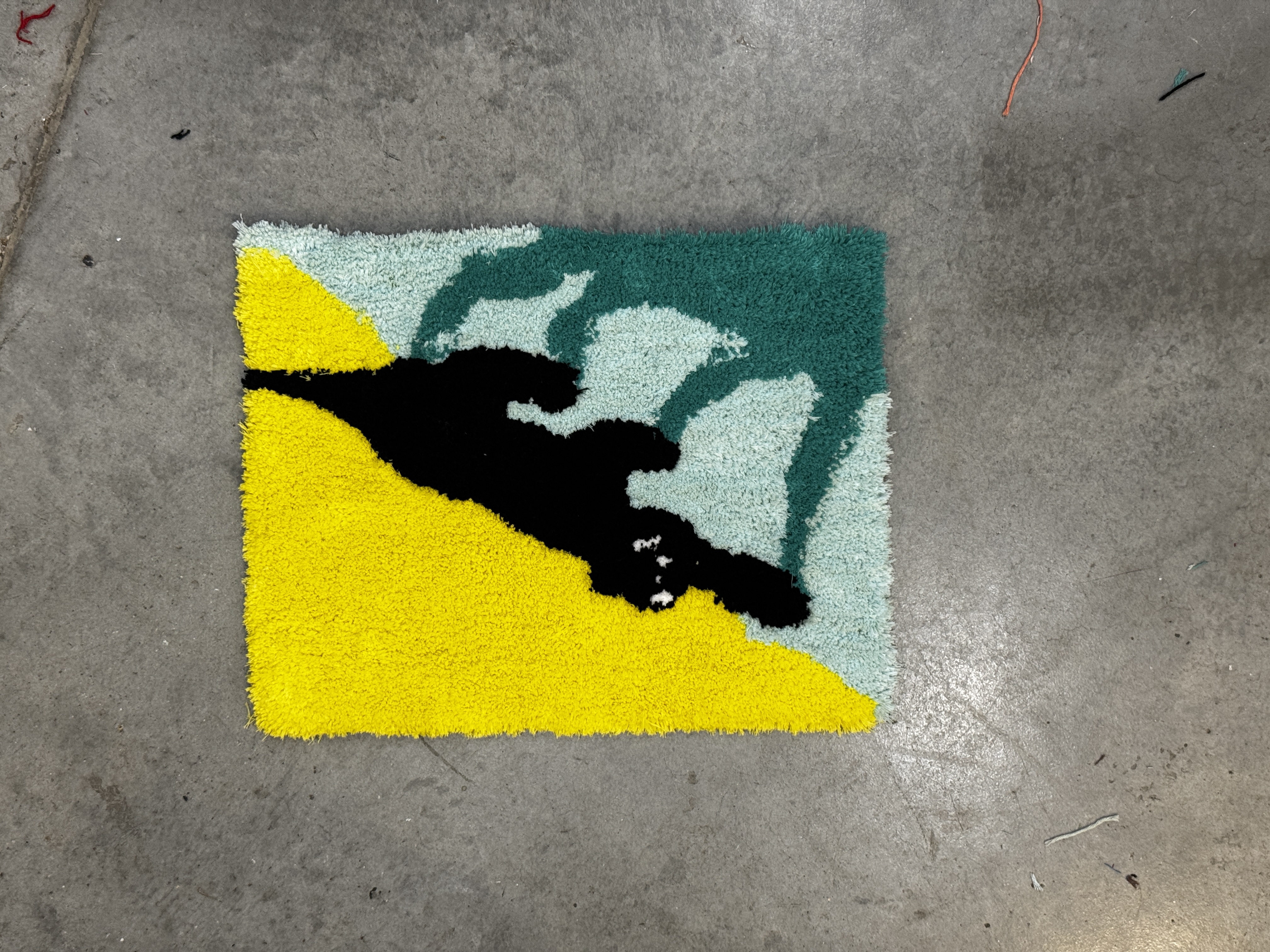 Square rug with a black cat design on a yellow and green background on a concrete floor.