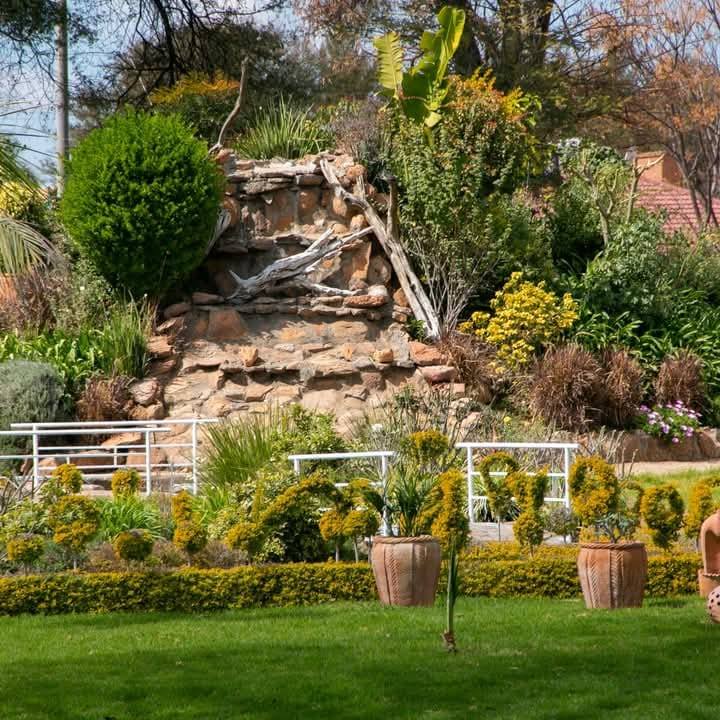 Well-maintained garden with green lawn, ornamental shrubs, potted plants, and a decorative stone rock wall with driftwood pieces.