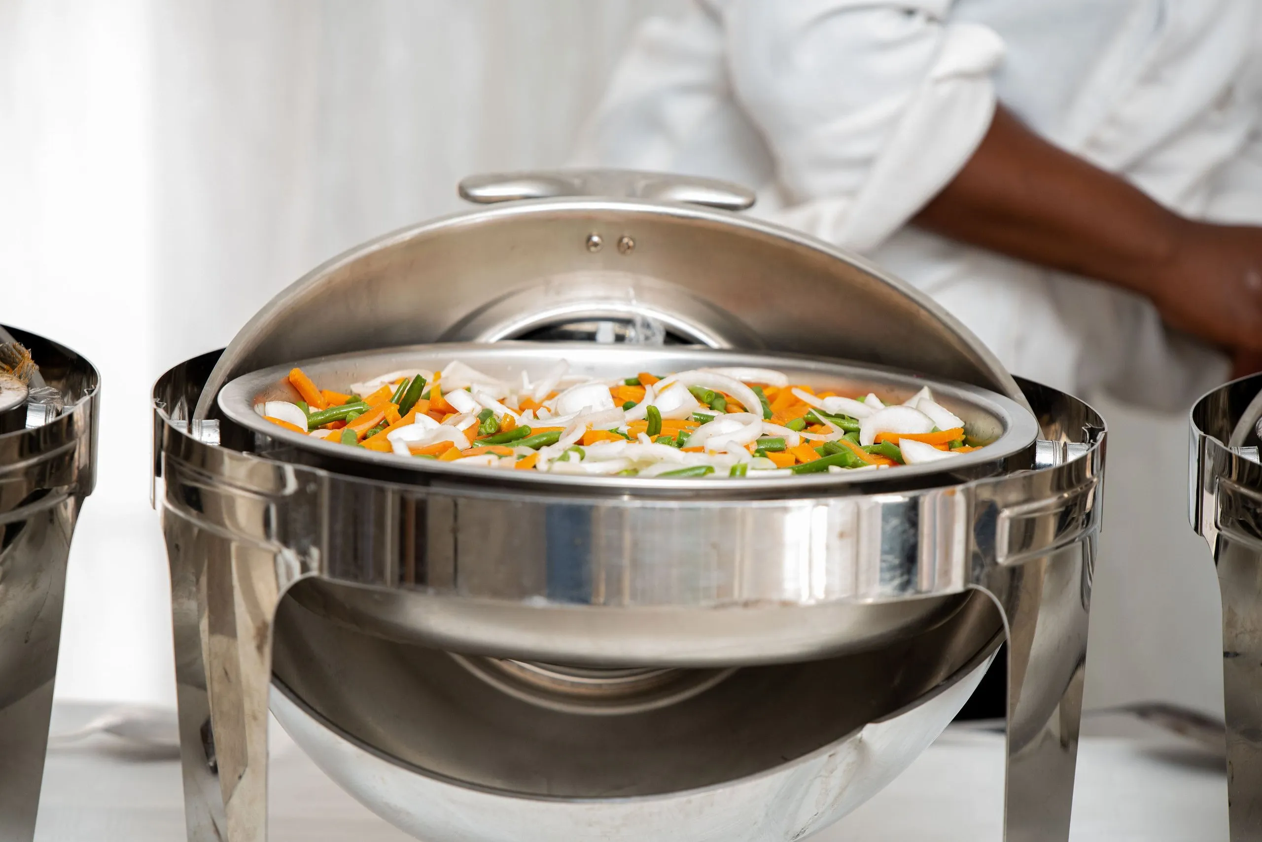 Chafing dish filled with cooked mixed vegetables including sliced onions, green beans, and carrots.