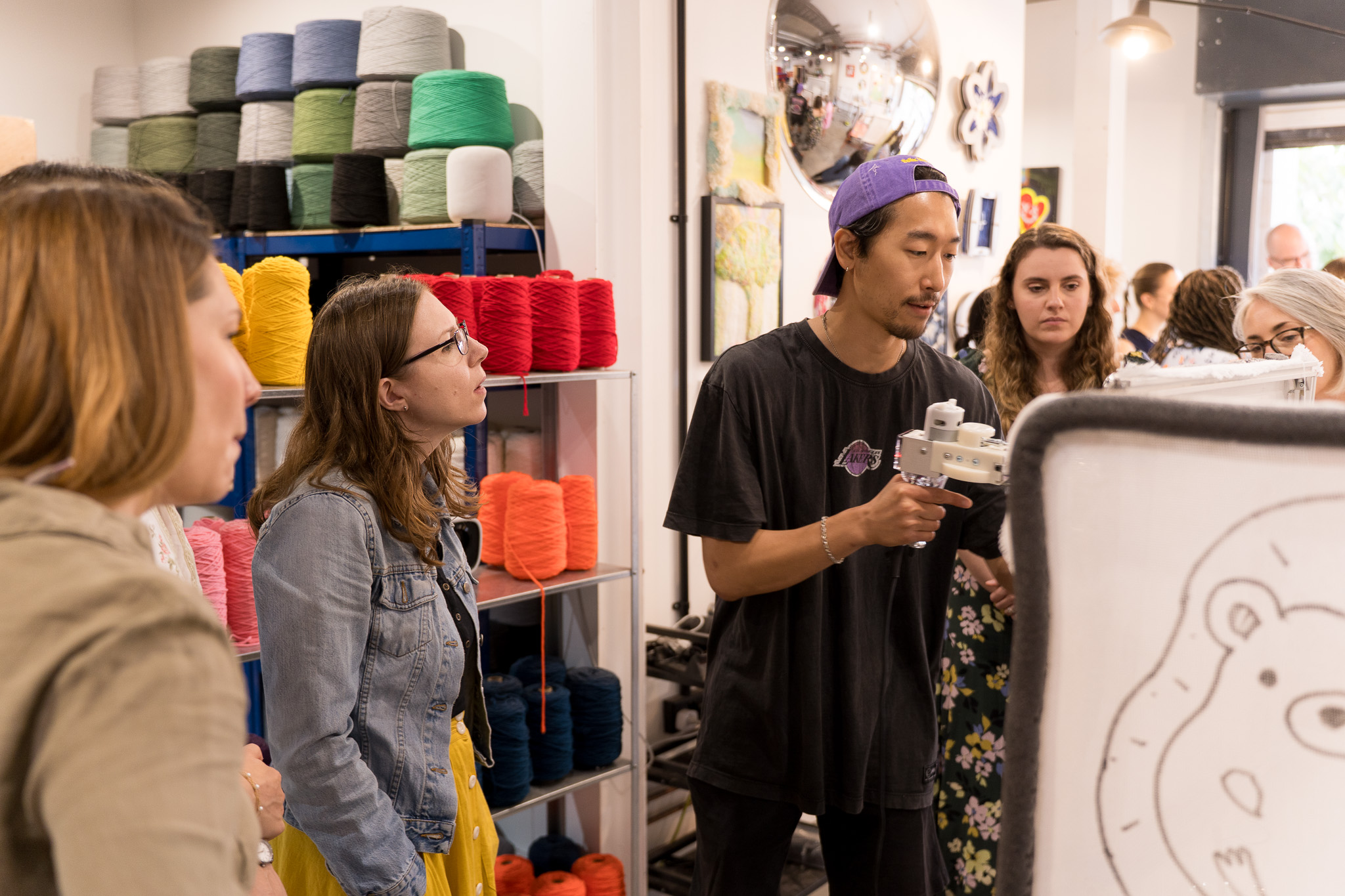 Cheeky Studio instructor demonstrating a tufting gun to workshop participants in Hackney Wick, London, with colourful yarn shelves in the background