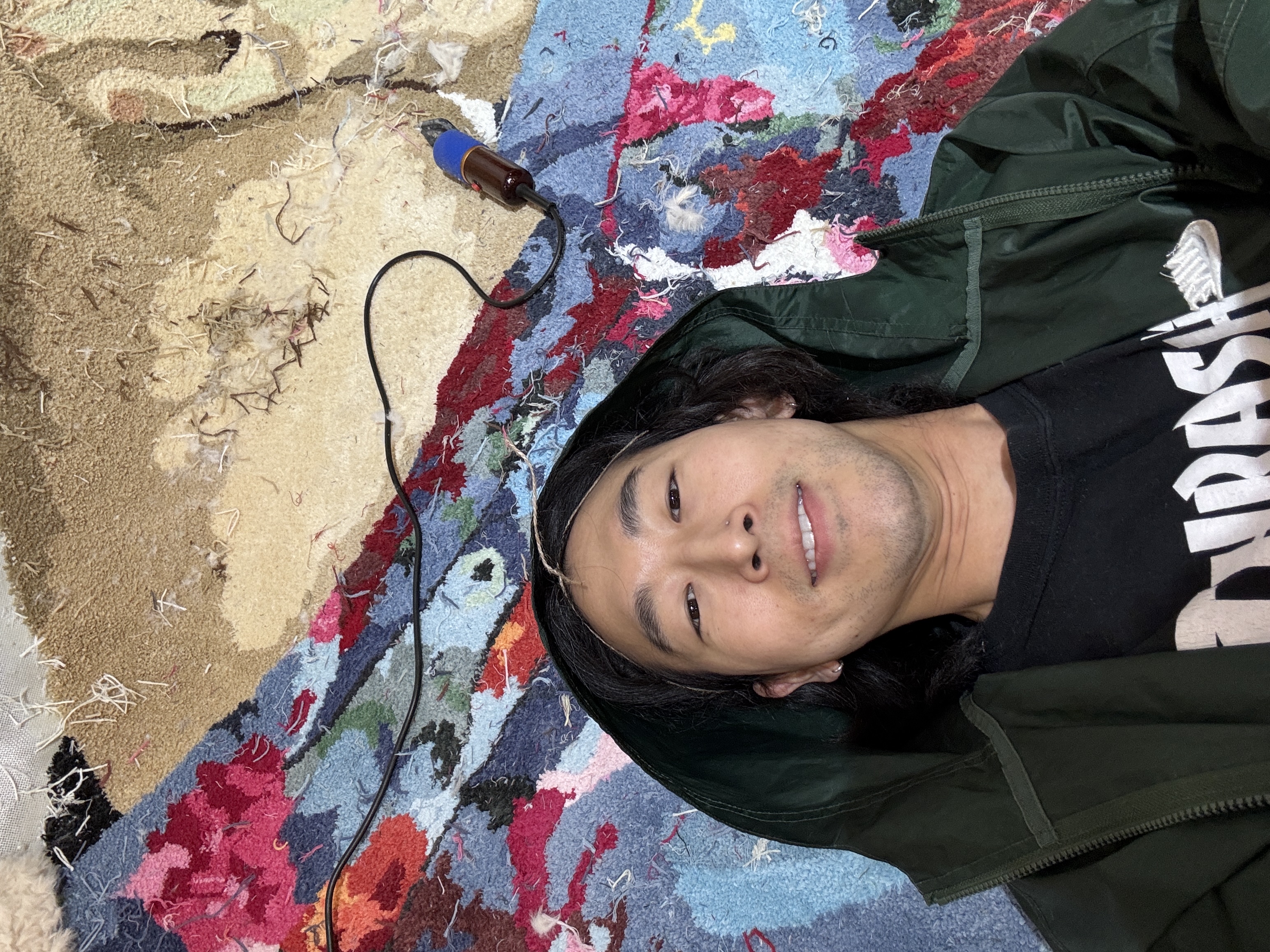 Jaymond Ahn, founder of Cheeky Studio, lying on the  completed 3×6m Danny Dyer tufted rug commission made  for Sky's Mr Bigstuff launch campaign, Hackney Wick London