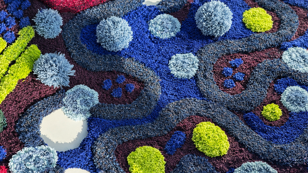 Macro detail shot of an abstract, highly textured hand-tufted rug featuring organic winding patterns in deep blue and plum, accented with raised 3D yarn pom-poms in lime green and light blue, showcasing advanced tufting and carving techniques at Cheeky Stu