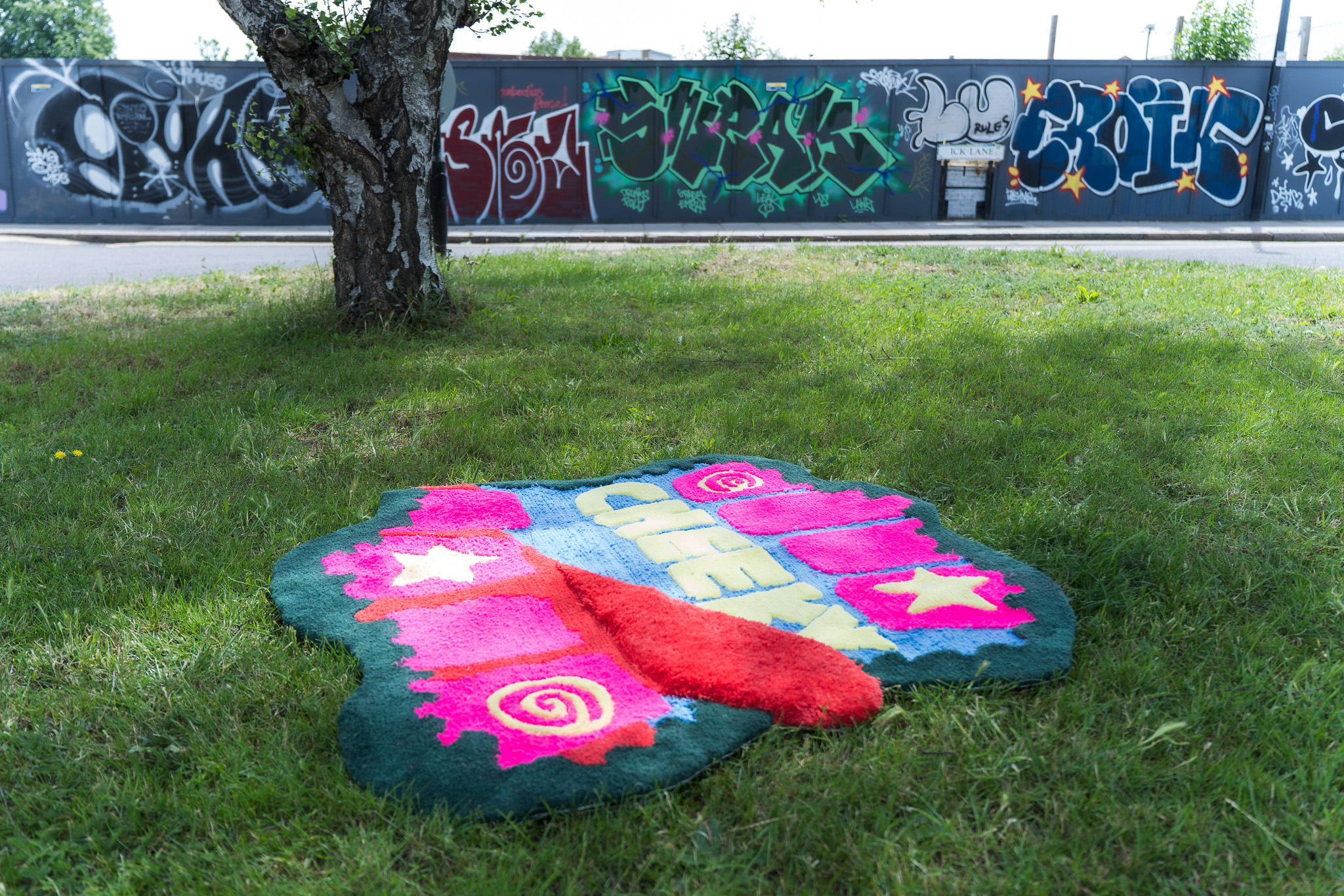 The Cheeky Studio floor rug laid on grass under a tree in Hackney Wick, with a graffiti wall behind