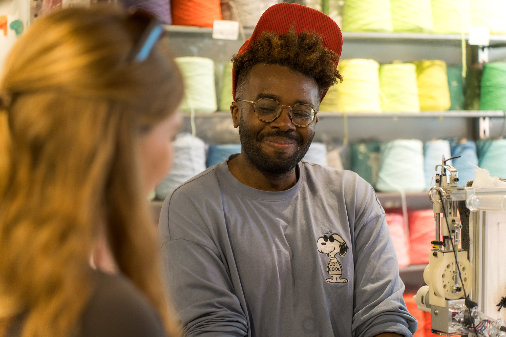 Smiling participant at a tufting frame during a team building session at Cheeky Studio, with rainbow yarn shelves behind