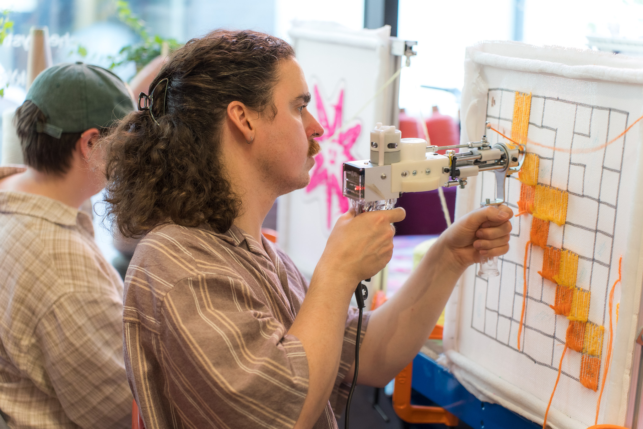 Participant tufting an orange grid design with a tufting gun at a Cheeky Studio team session