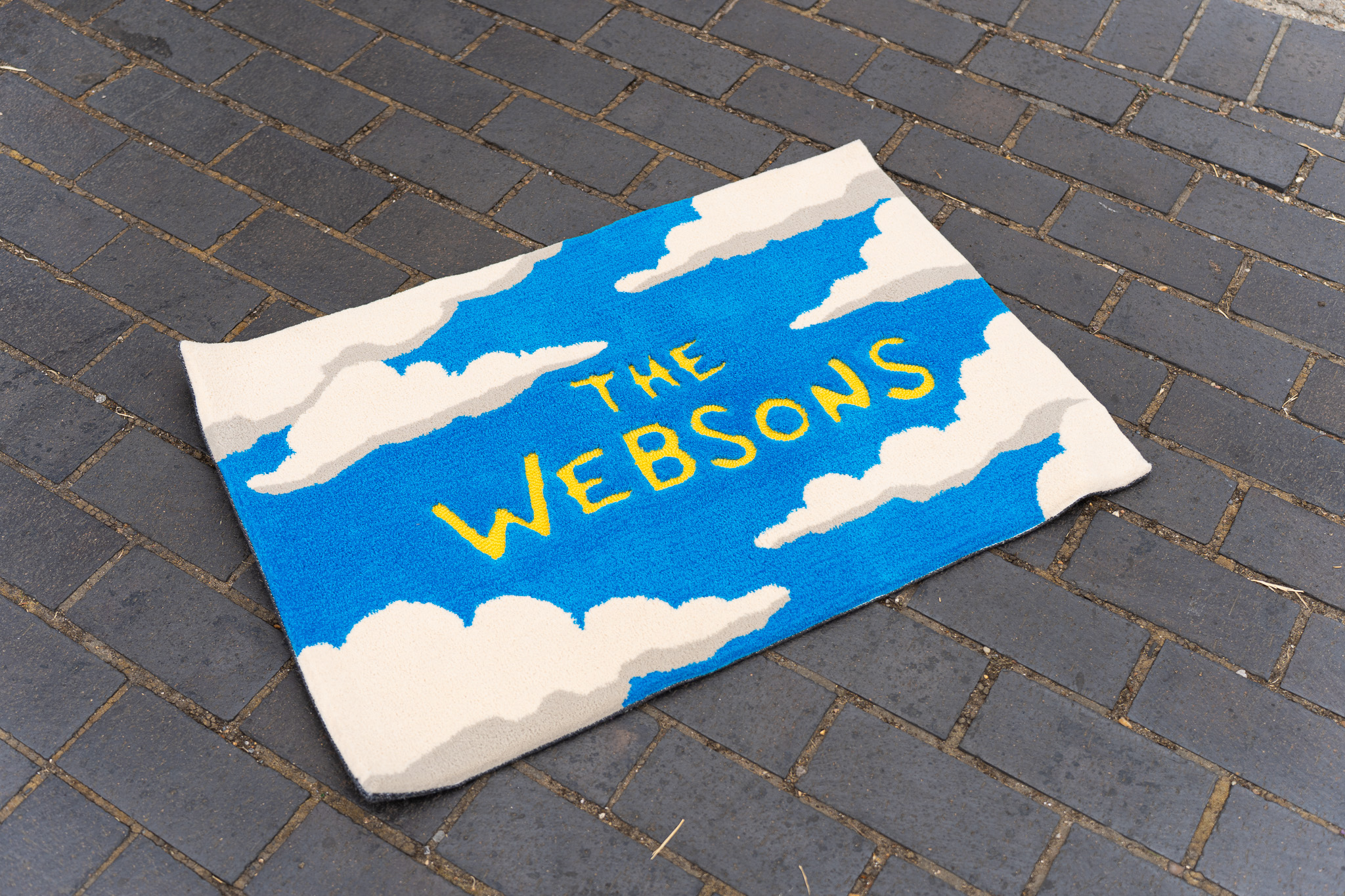 Blue and cream custom tufted rug with yellow The Websons lettering, handmade by Cheeky Studio in London