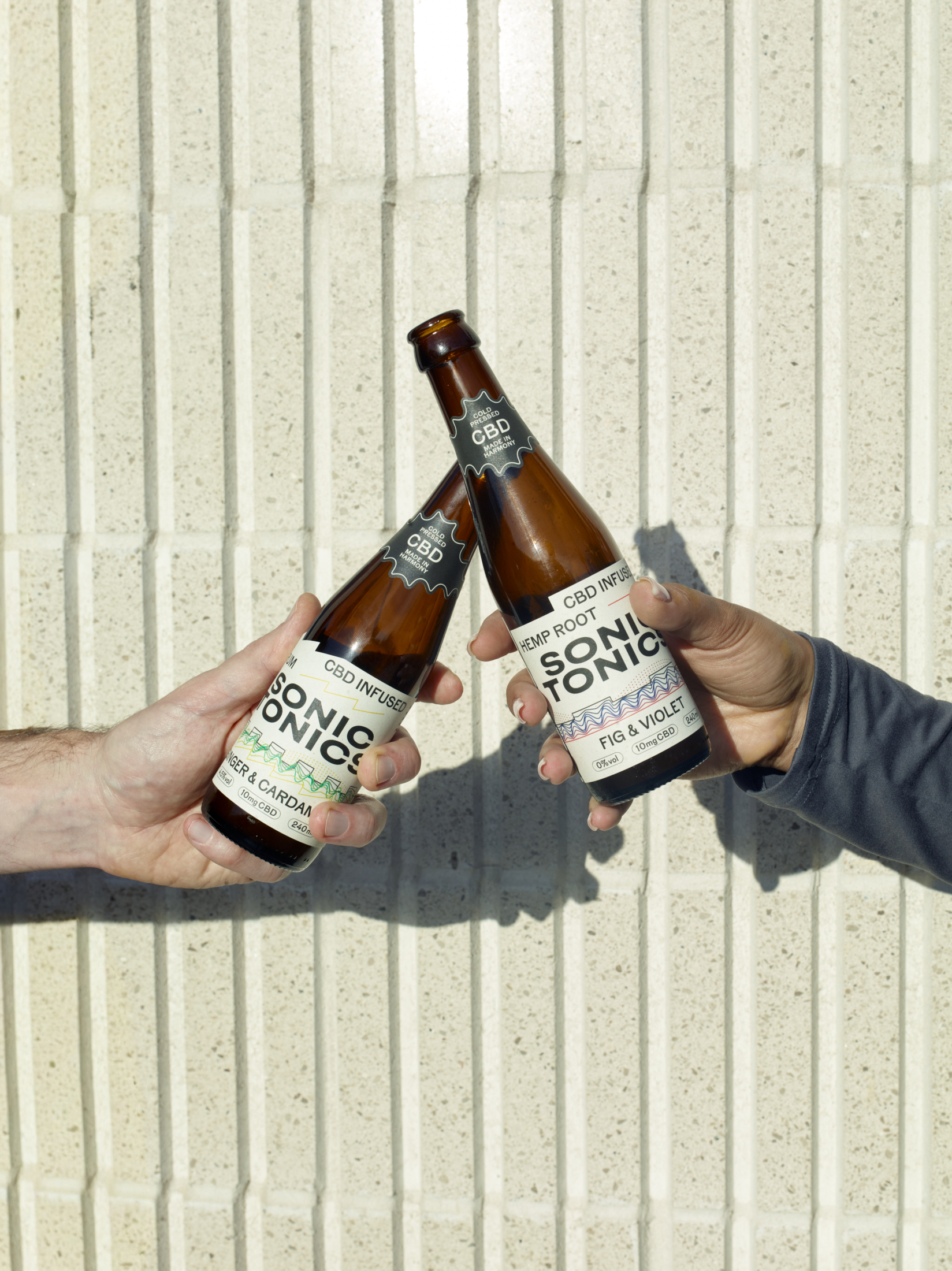 Two people holding Sonic Tonics Ginger and Cardamom and alcohol-free Fig and Violet CBD-infused drinks