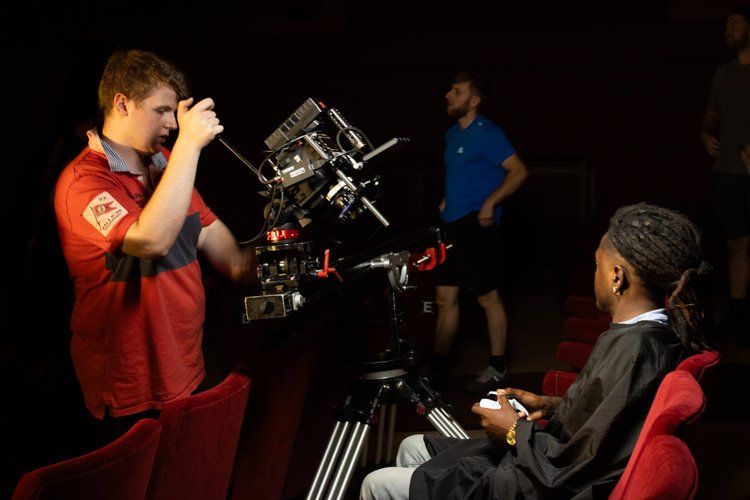 A Vault 5 Studios cinematographer adjusts a professional camera setup on location. Crew members stand in the background, highlighting the collaborative, human-first approach to film production.