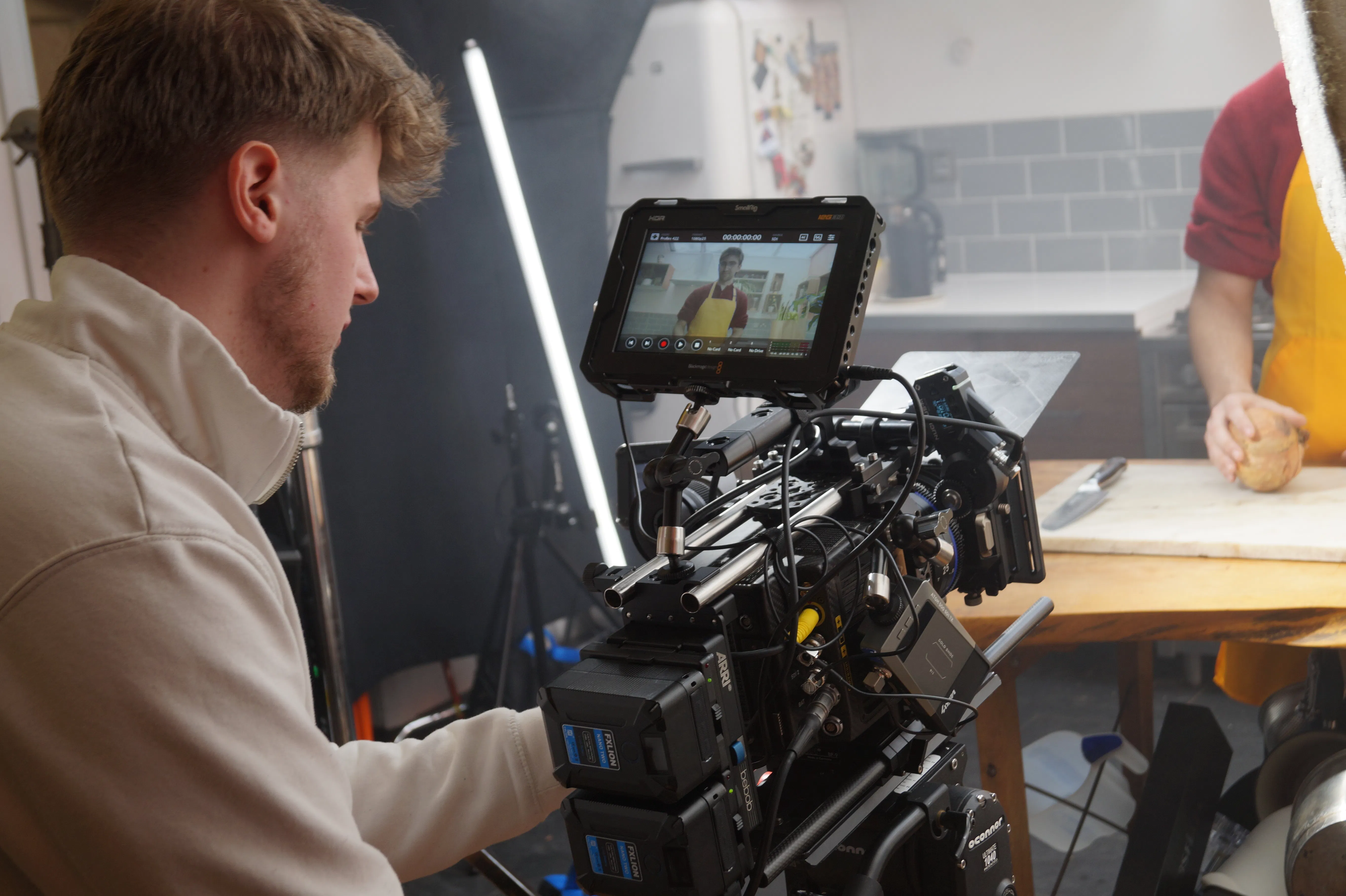 A Vault 5 Studios crew member operates a cinema camera, capturing a scene in a kitchen. Studio lighting and filming equipment are visible, showing an authentic brand story production.