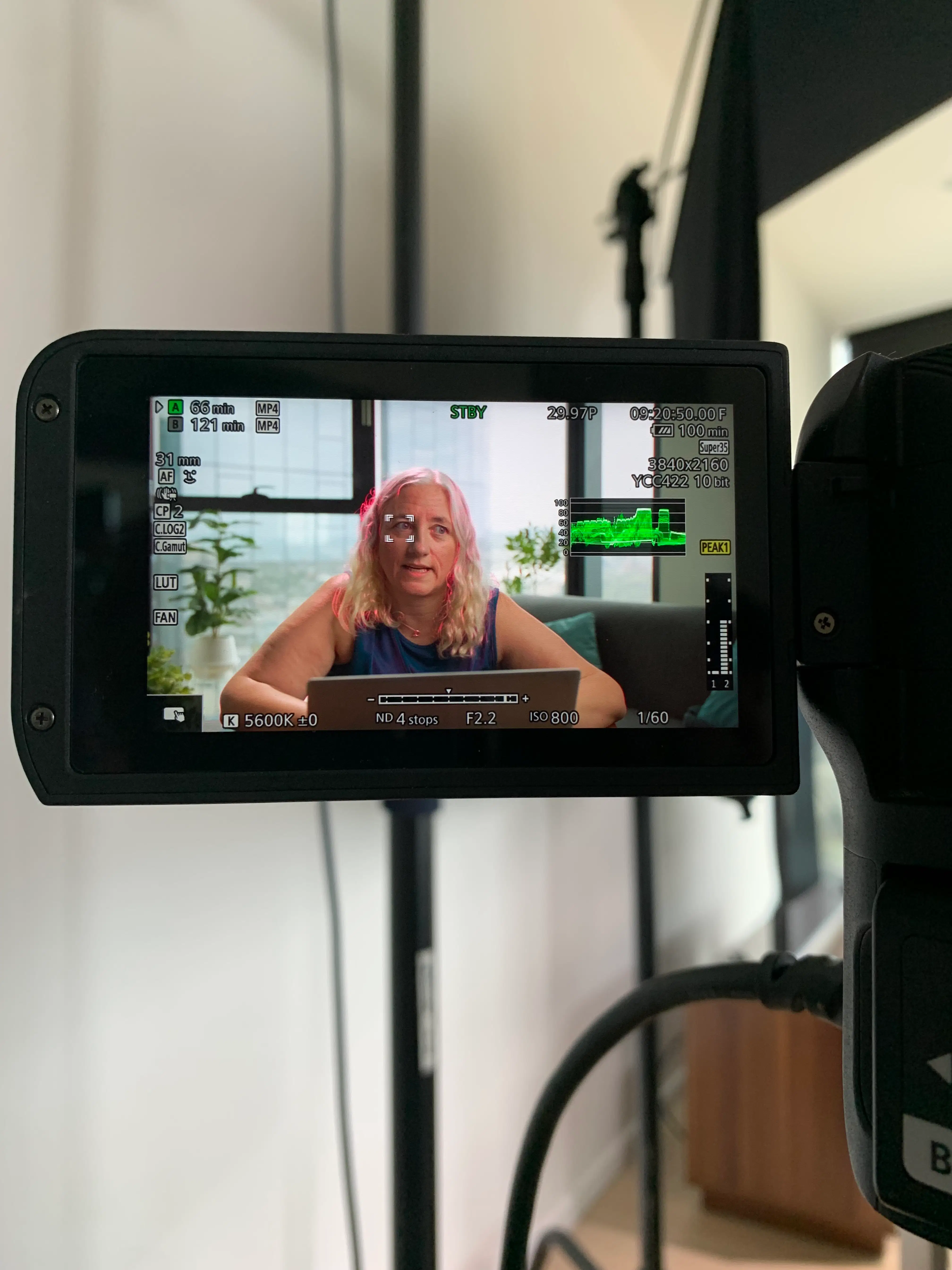 A behind-the-scenes view of a Brand Story interview being filmed at Vault 5 Studios. The camera screen shows an interviewee speaking authentically toward the lens in a natural light setting.