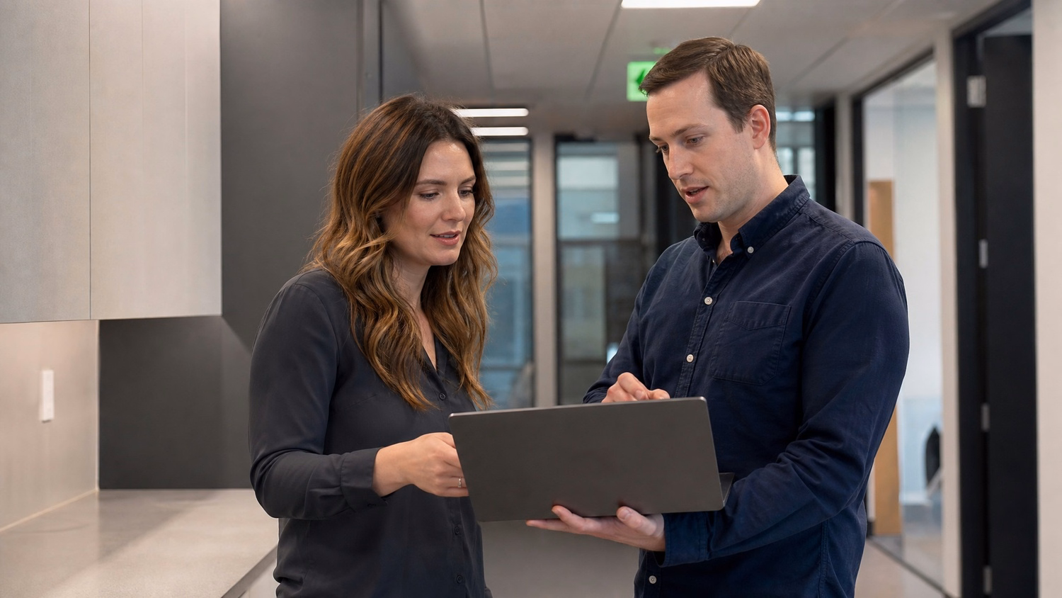 INFORMAL HUDDLE An IT professional  two people standing and talking near a ki