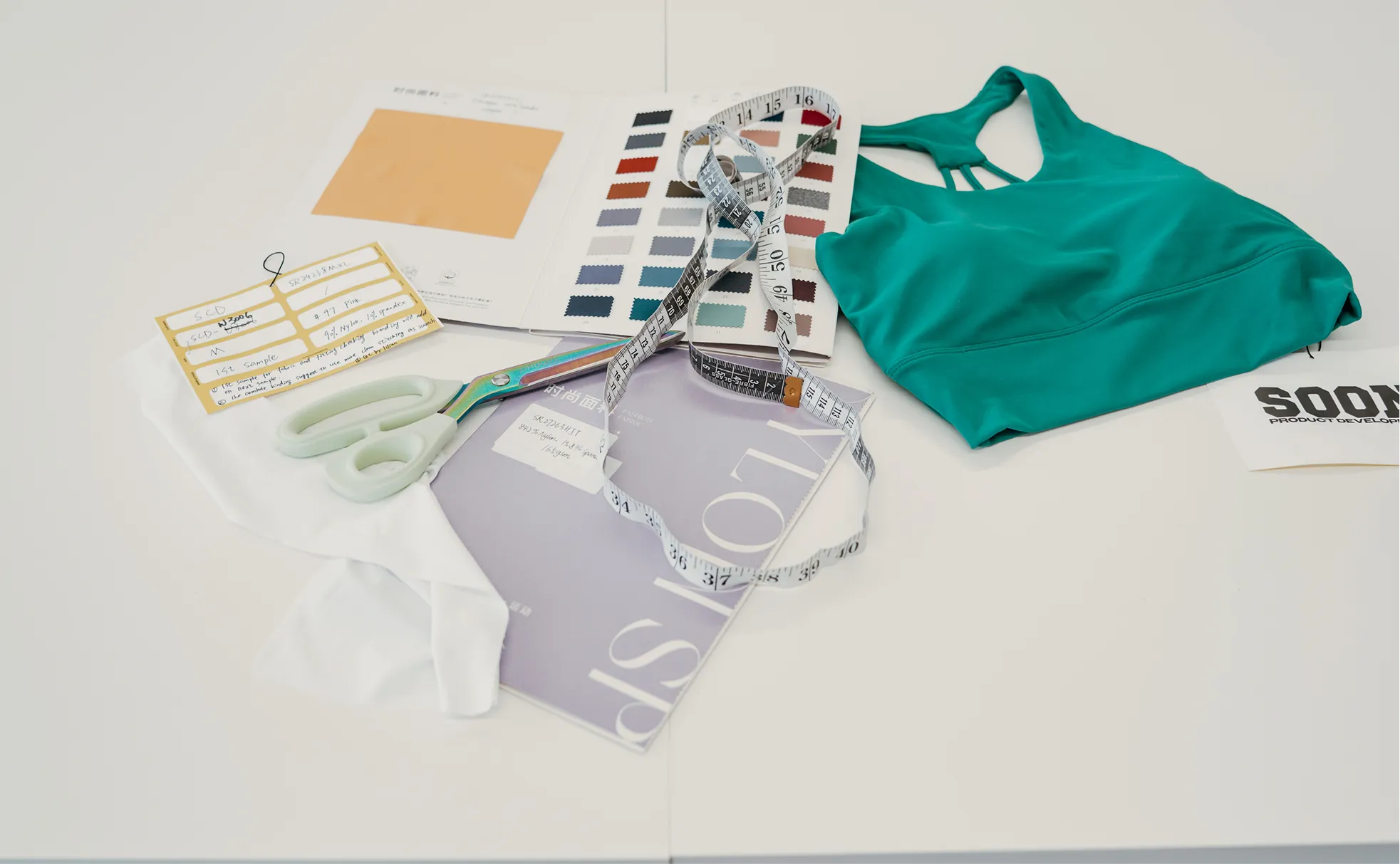 Green sports bra, fabric swatches, measuring tape, scissors, and notes on a white table.