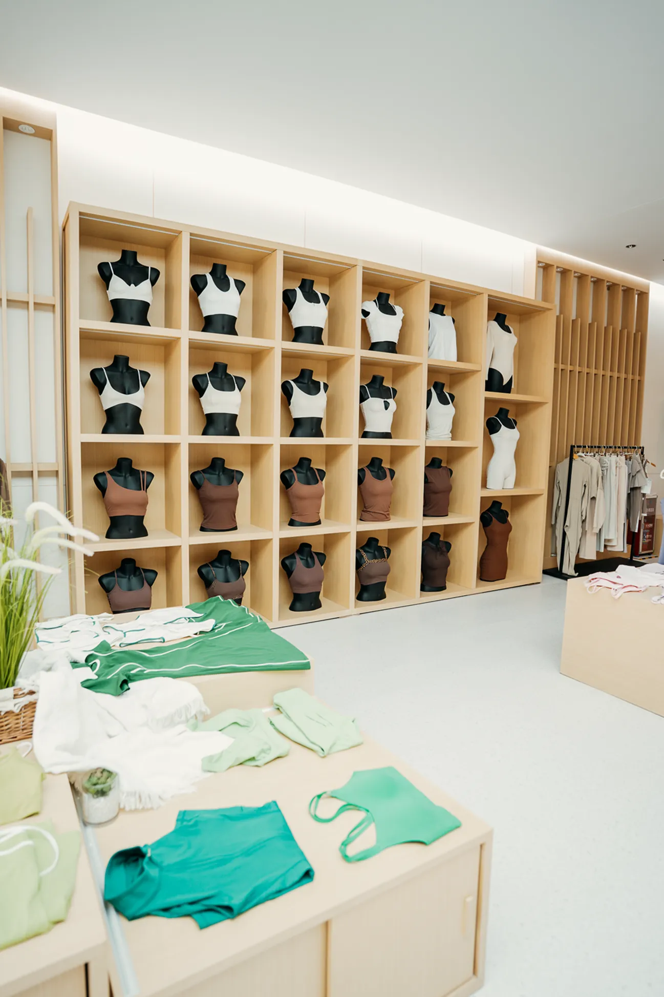 Clothing store display with black mannequins wearing white and brown tops and green activewear on tables.